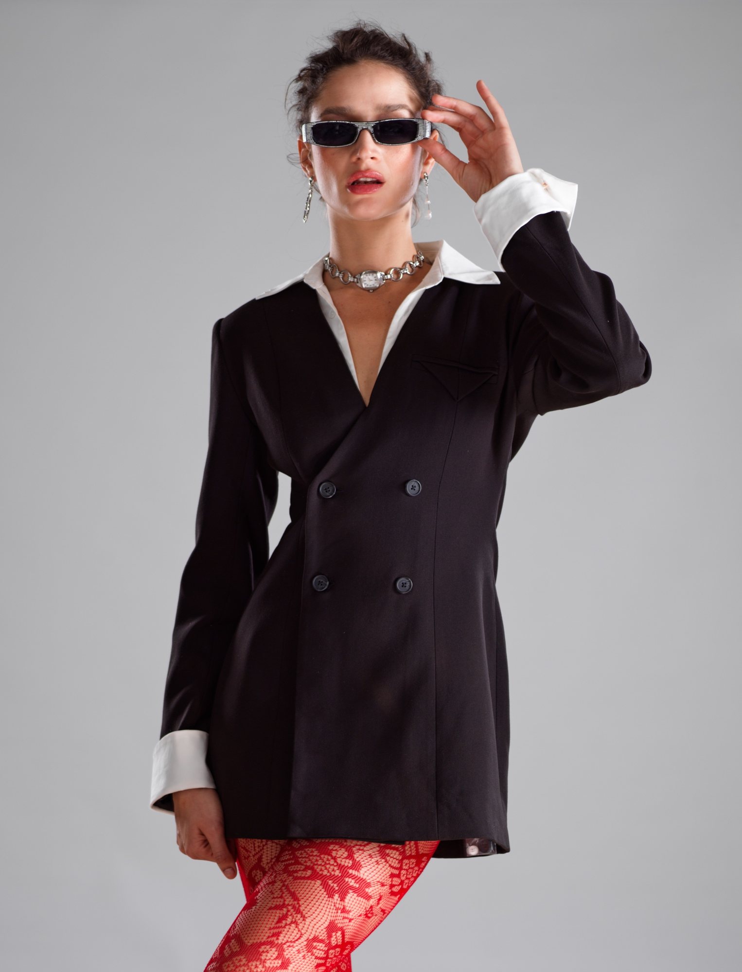 Model in a black double-breasted blazer with white collar and cuffs, sunglasses, a silver watch choker and red lace tights