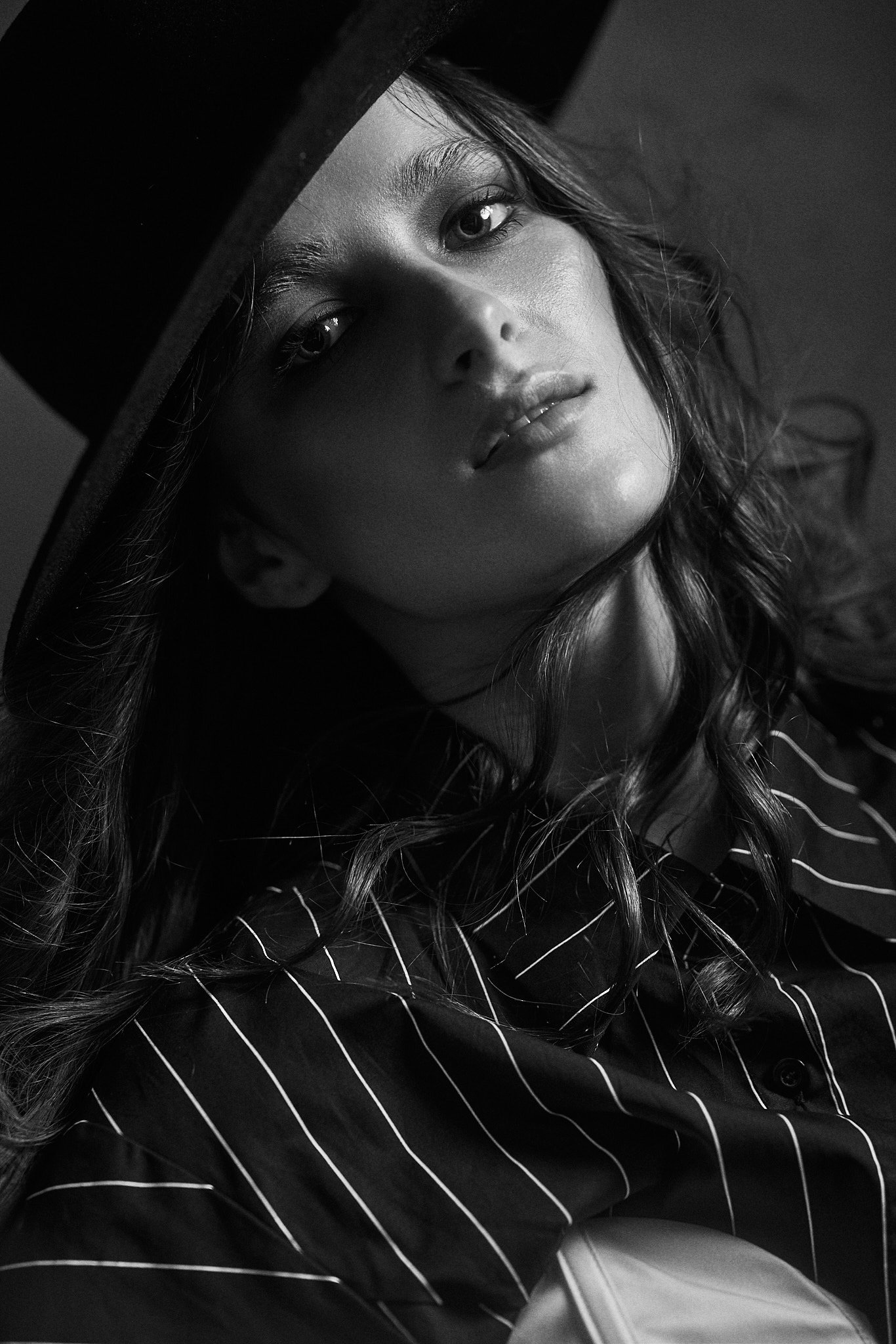 Black and white close-up portrait of a model in a wide-brimmed black hat and pinstripe shirt